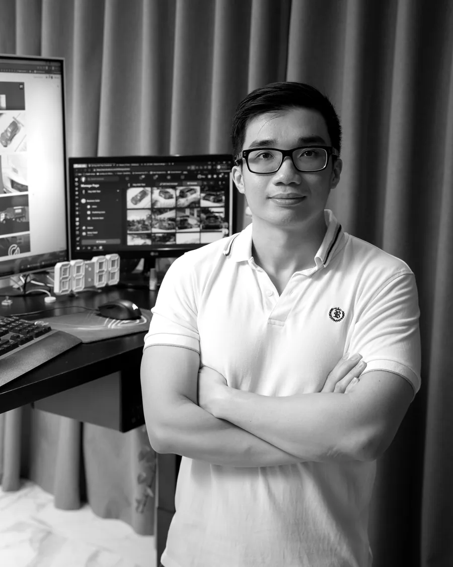 Huy Anh Tran at his desk, arms crossed, car projects on the screens behind him